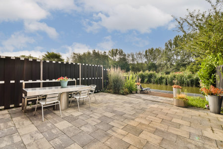 An inviting outdoor patio with a modern table and chairs, surrounded by greenery and a serene waterway. Perfect for relaxation and gatherings.の写真素材