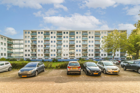 A sleek modern residential building surrounded by greenery, featuring a parking lot with various cars under a clear sky. Ideal for architectural showcases.の写真素材