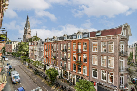 A picturesque view of an Amsterdam street featuring traditional brick buildings, trees lining the road, and a stunning church spire in the background.の写真素材