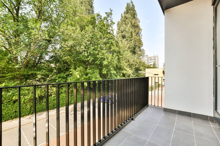 A modern balcony reveals a scenic view of vibrant trees and a well-maintained street, providing a tranquil outdoor space for relaxation.の写真素材