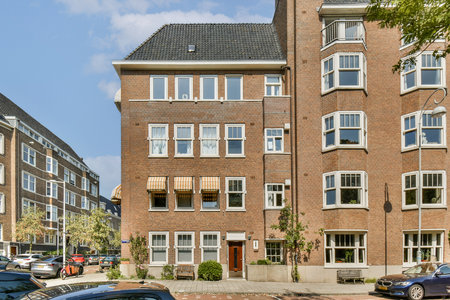 A picturesque brick building features large windows and distinctive architectural elements, surrounded by trees and cars in a vibrant urban environment.の写真素材