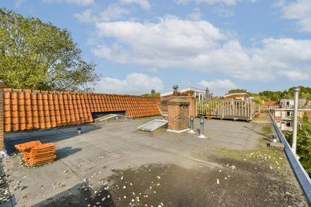 A rooftop scene featuring a mixture of roofing materials and lush greenery under a partly cloudy sky, showcasing urban architecture and natures presence.の写真素材