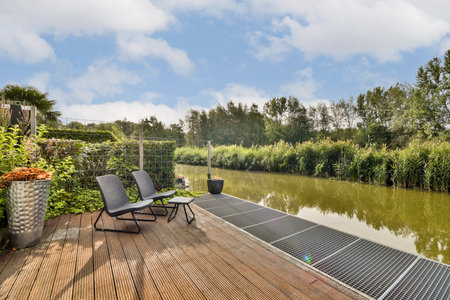 A peaceful riverside setting featuring comfortable seating, lush greenery, and tranquil water,...