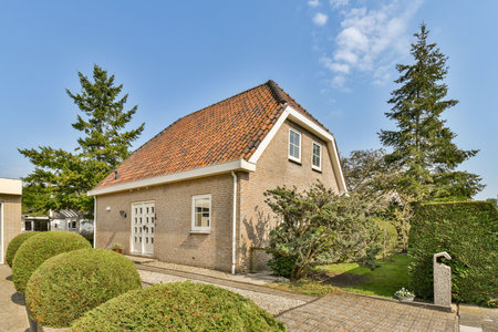 A picturesque modern house featuring a sloped roof, surrounded by lush greenery and neatly trimmed hedges, under a clear blue sky.の写真素材