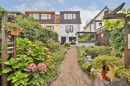 A picturesque view of a garden pathway lined with blooming flowers, leading to modern houses with glass windows, showcasing tranquility and charm in a residential area.の写真素材