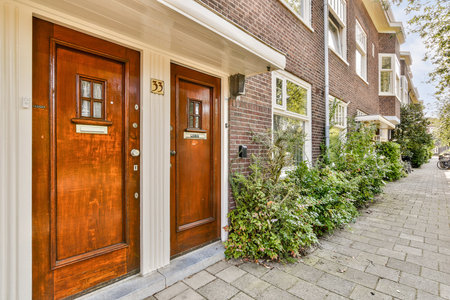 A picturesque view of an inviting brick building featuring two wooden doors, surrounded by lush green foliage and a charming sidewalk.の写真素材