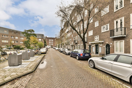 A serene urban street scene showcasing parked cars lined along a cobblestone road, framed by residential buildings and trees under a partly cloudy sky.の写真素材