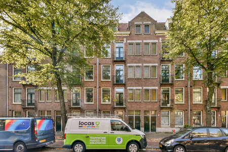 A picturesque urban landscape showcasing a charming building adorned with large windows, framed by vibrant trees and parked vehicles, capturing suburban tranquility.の写真素材