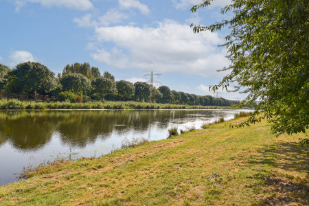 A tranquil river scene featuring lush greenery along the banks, reflecting the clear blue sky and fluffy clouds, creating a peaceful atmosphere.の写真素材