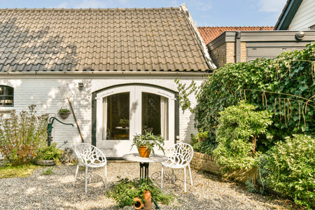 A cozy outdoor patio featuring white chairs and a small table surrounded by lush green plants. The inviting space is ideal for relaxation and leisure moments.の写真素材
