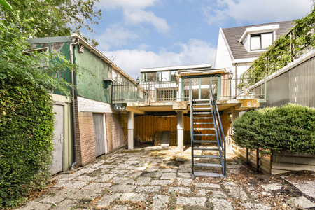 An inviting outdoor area featuring a staircase leading to a balcony, surrounded by greenery and a mixture of modern and rustic architecture.の写真素材