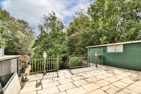A vibrant outdoor area featuring lush trees and a modern green structure, surrounded by a stone patio and decorative fencing, perfect for relaxation.の写真素材