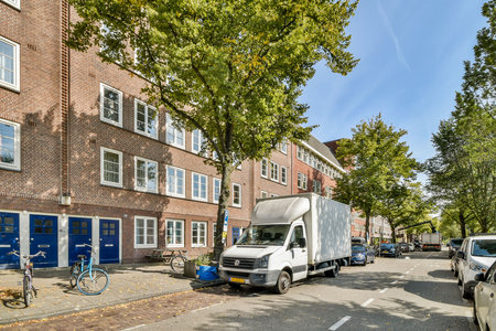 A scenic street featuring a mix of modern and historic buildings, lined with trees and parked vehicles, showcasing urban life and architecture.の写真素材