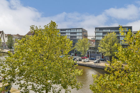 A vibrant urban scene showcasing modern buildings along a serene waterway, bordered by lush greenery and reflective waters. Perfect for city and nature lovers.の写真素材