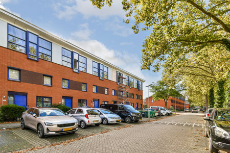 A picturesque view of a residential street featuring modern brick buildings and parked cars under a clear blue sky, surrounded by lush trees.の写真素材