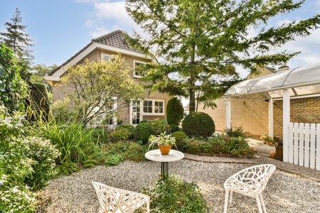 A picturesque scene featuring a rustic house surrounded by lush greenery, well-kept garden space, and cozy outdoor seating, perfect for relaxation.の写真素材