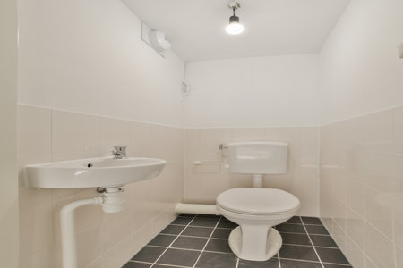 A clean, minimalist bathroom featuring a white wall-mounted sink and a modern toilet, complemented by sleek tiles and efficient lighting.の写真素材