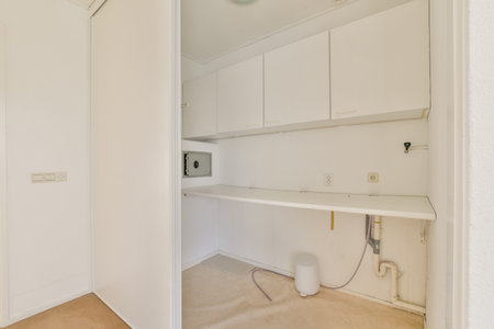 A clean and minimalist laundry room featuring white cabinetry and a simple layout. The design emphasizes functionality and simplicity, ideal for modern living.の写真素材