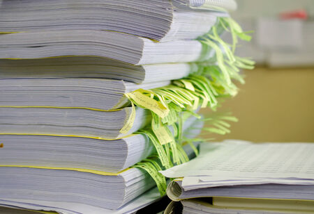 Pile of documents on desk stack up high waiting to be managed.の写真素材