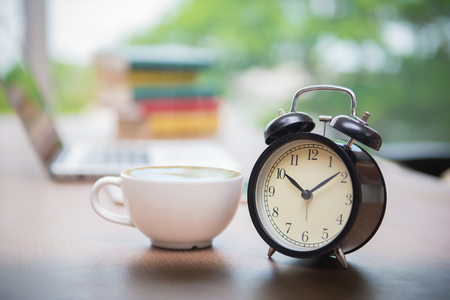 Retro alarm clock with cup of cappuccino on table in office, Coffee Break time.の写真素材