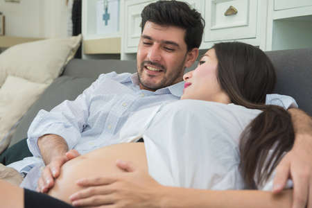 pregnant woman and husband are happy couple expecting a baby on sofa.の写真素材