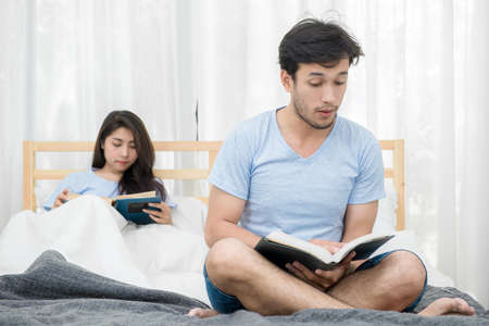 young loving couple reading a book on bedroom at homeの写真素材