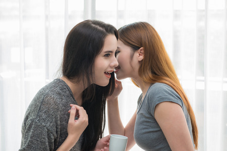 Beautiful girls with friend talking and holding coffee cups in living room at home.の写真素材