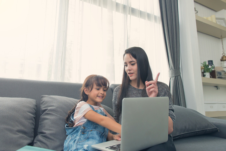 Beautiful young mom and daughter are using notebook on sofa at home.の写真素材