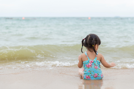 little girl sitting and playing on the beach with sand.の写真素材