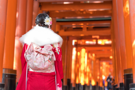 Woman dressed in traditional japanese costume walking under Red Tori Gate of Fushimi Inari Taisha Kiyomizu-dera Temple in Kyoto Japan.のeditorial素材