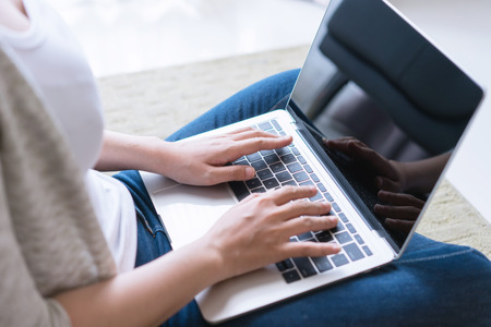 Young woman working on a laptop sitting on sofa at home.の写真素材