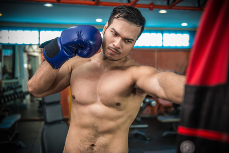 Handsome muscular man in boxing gloves punching bags in gym.の写真素材