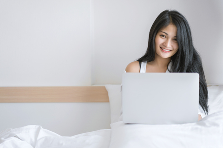 Young woman working on a laptop sitting on bed at home.の写真素材