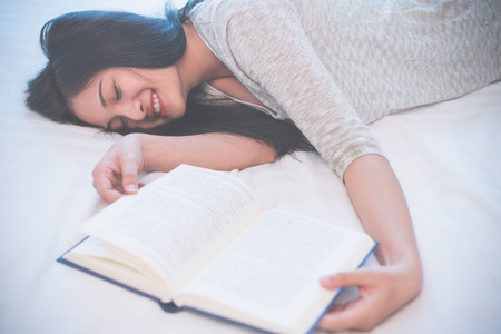 Young woman reading a book on bed at home.の写真素材