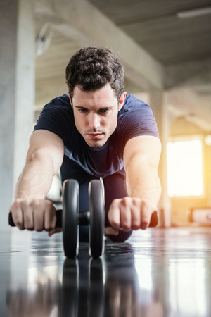Athlete sporty man doing exercise with abs roller wheel to strengthen his abdominal muscle in gym.の写真素材