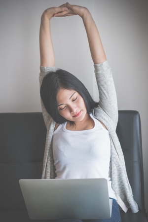 Young woman working on a laptop sitting on sofa at home.の写真素材
