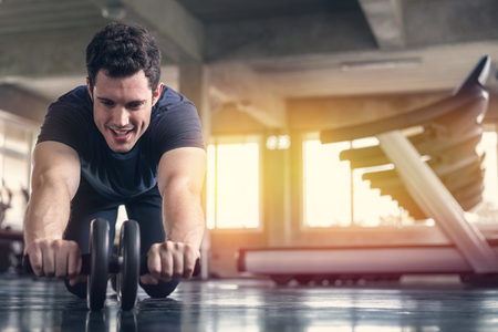 Athlete sporty man doing exercise with abs roller wheel to strengthen his abdominal muscle in gym.の写真素材