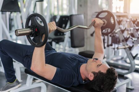 Handsome weightlifter lifting barbells bench press working out with curl bar in the gym.