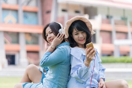 Two Young woman enjoying music in the garden listening to music with headphones.の写真素材