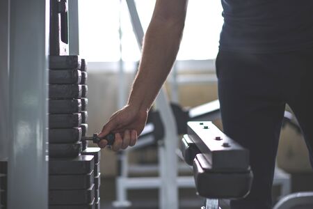 Handsome hand change weight on Iron heavy plates stacked of weight machine in gym.の写真素材