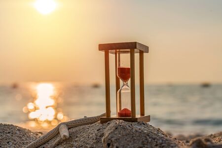 Time concept Hourglass and Starfish on sandy beach in summer with sea background.