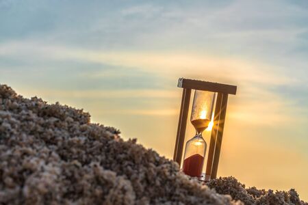 Time concept Hourglass on sandy beach in summer with sea background.