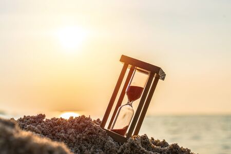 Time concept Hourglass on sandy beach in summer with sea background.