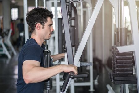 Handsome man lowering weight of fitness machine and working out in the fitness gym.