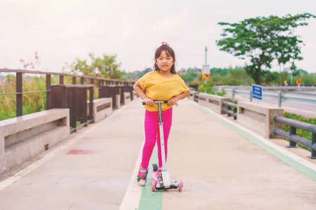 Little child girl to ride scooter in outdoor sports ground on sunny summer day. Active leisure and outdoor sport for children.の写真素材