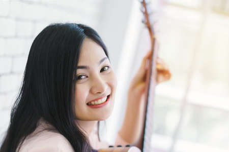 young woman playing guitar in living room, Enjoying carefree time at home.の写真素材