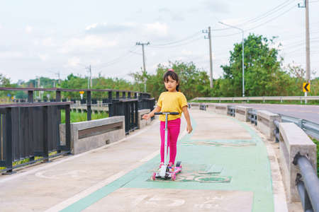 Little child girl to ride scooter in outdoor sports ground on sunny summer day. Active leisure and...