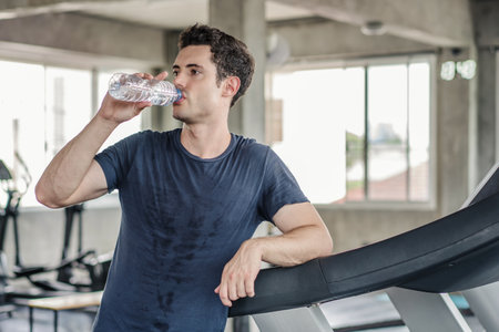 Handsome man drinks water in gym. Sports nutrition concept.