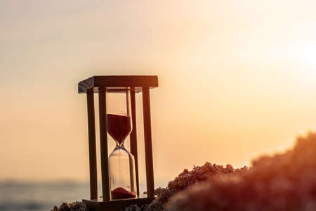 Time concept Hourglass on sandy beach in summer with sea background.の写真素材