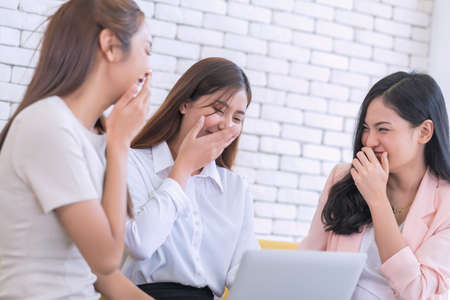Beautiful young business women are looking on website by laptop at living room. Happy friendship...